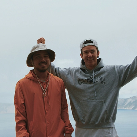 Deux jeunes hommes souriants devant un paysage naturel, incarnant l’esprit collectif d’une entreprise à impact tournée vers la nature et les projets humains