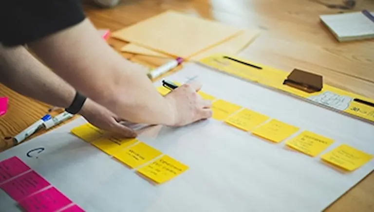 Personne organisant des notes sur un tableau blanc, symbolisant la planification efficace d’une campagne de crowdfunding