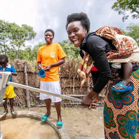 Femmes souriantes utilisant une pompe à eau dans un village, illustration d’un projet de création de puits pour faciliter l’accès à l’eau