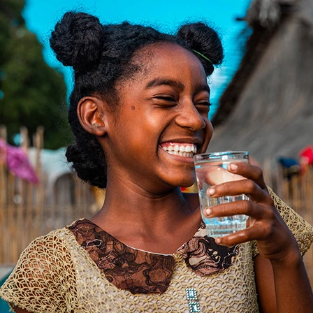 Jeune fille souriante tenant un verre d’eau potable, illustration de l’impact des collectes de fonds sur l’accès à l’eau