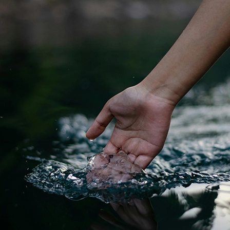 Main touchant la surface de l’eau, symbole de l’engagement sensible d’une entreprise à impact pour la préservation de la ressource