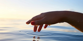 Main effleurant la surface de l’eau au coucher du soleil, symbole de l’engagement à travers un don