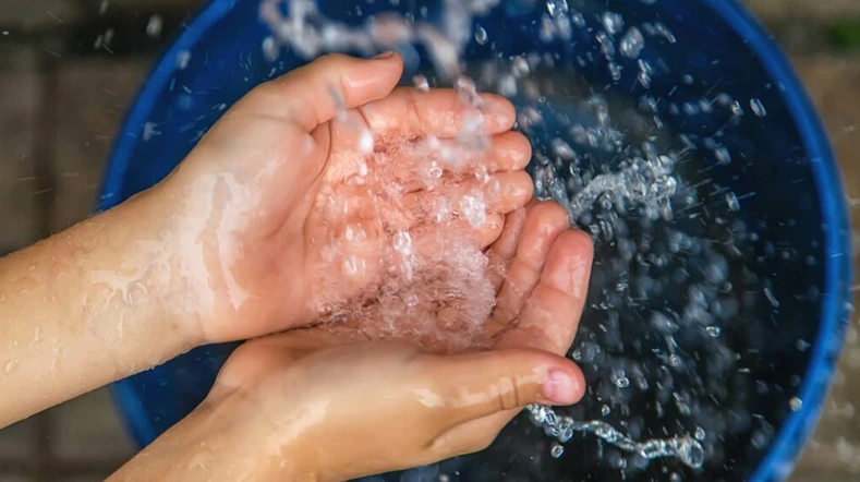 Mains d’un enfant recevant de l’eau claire, résultat concret du projet de puits en cours